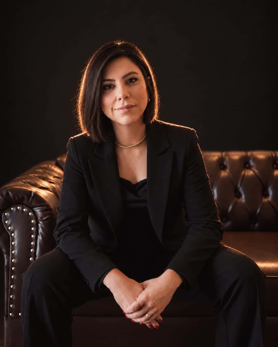 Simone Tatiana da Silva, advogada, sentada em um sofá de couro, em blazer preto, olhando para a câmera